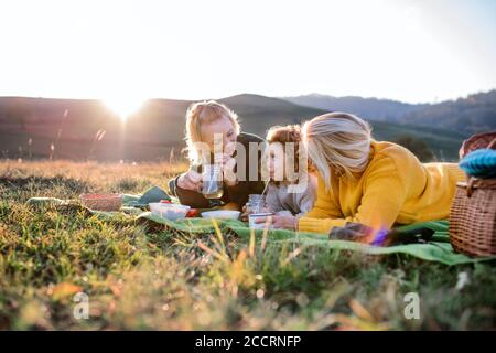 Small girl with mother and grandmother having picnic in nature at sunset. Stock Photo