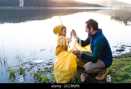 Father with small daughter collecting rubbish outdoors in nature, plogging concept. Stock Photo