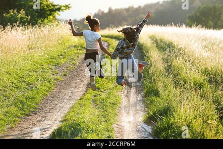 Rear view of young teenager girls friends outdoors in nature, jumping. Stock Photo