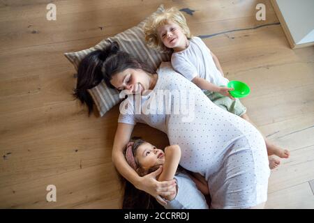 Top view of pregnant woman with small children indoors at home, lying on floor. Stock Photo