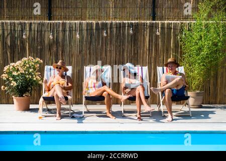 Group of cheerful seniors sitting by swimming pool outdoors in backyard. Stock Photo