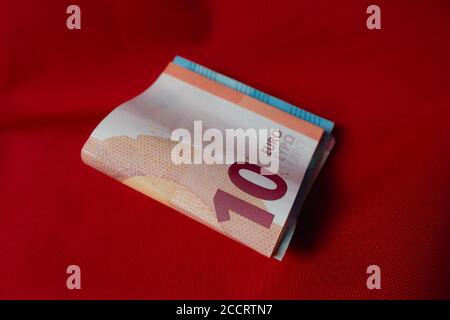 Money bundle with a 10 Euro note on top, lying on a red background Stock Photo