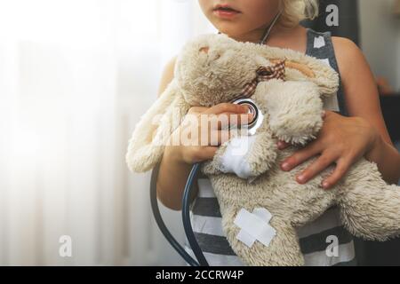 child playing doctor with soft toy. girl examining bunny with stethoscope at home