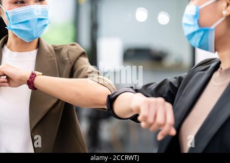 Close up two businesswomen do alternative greeting in new normal office lifestyle. They wear protective face mask and use elbow touch instead of hand Stock Photo