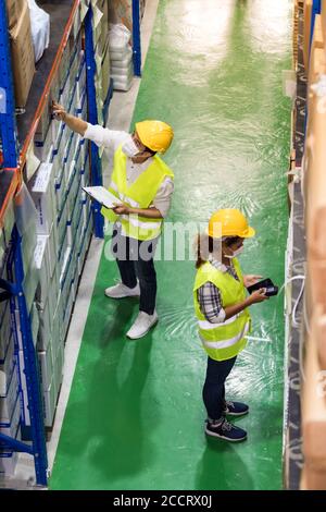 Asian and African black warehouse workers with face mask checking goods use clipboard barcode scanner in distribution center. Storeroom business wareh Stock Photo