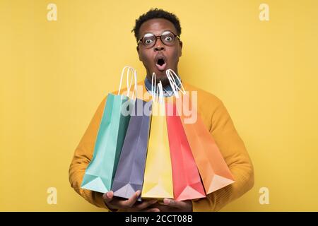 Shocked african young man holding shopping bags being surprises. Stock Photo