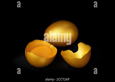Golden eggs and half broken egg with yolk isolated at the black background Stock Photo