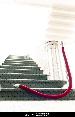 Over exposed, heavenly light at top of ascending staircase; with selective focus on red velvet rope opened on the floor - granting access to the myste Stock Photo