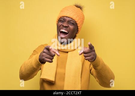 African man in yellow sweater and warm hat pointing at camera on joke Stock Photo