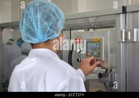Pharmaceutical industry an employee in a dressing gown and headdress stands at the control panel of an automated production line and manages productio Stock Photo