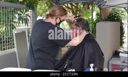 An older man is getting a haircut outside as Sports Clips hair salon moved operations outdoors to avoid Covid-19 shutdown. Stock Photo