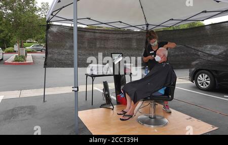 An older man is getting a haircut outside as Sports Clips hair salon moved operations outdoors to avoid Covid-19 shutdown. Stock Photo