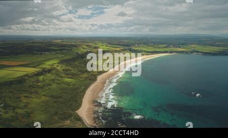 Beach aerial view panoramic landscape in Antrim County, Northern Ireland. Beautiful Atlantic Ocean coastline, green grass meadows and countryside stretch out to grey rain clouds. Stock Photo