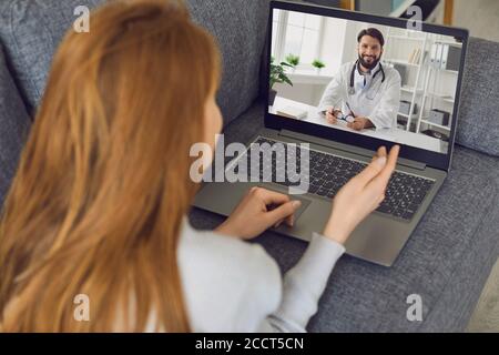 Woman lies on the couch at home and uses a laptop to call a doctor online. Stock Photo