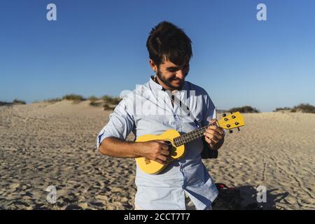 Young smiling male playing the ukulele at the beach Stock Photo