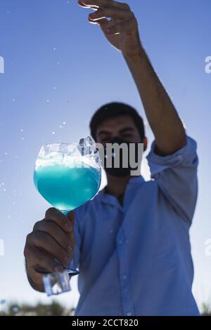 Vertical shot of a male dropping ice cubes into the cocktail Stock Photo