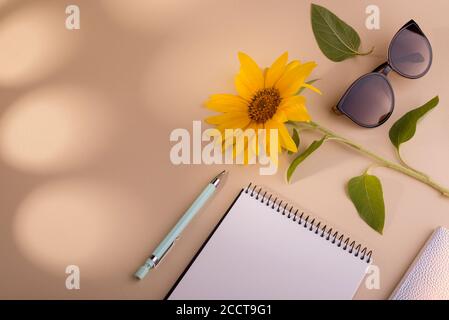 Fashion flat lay with notebook, sun glasses, sunflower, and pen against beige background. Good for summer sale advertising. Stock Photo