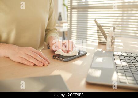 Close up pf unrecognizable woman sanitizing smartphone while working at desk in post pandemic office lit by sunlight, copy space Stock Photo
