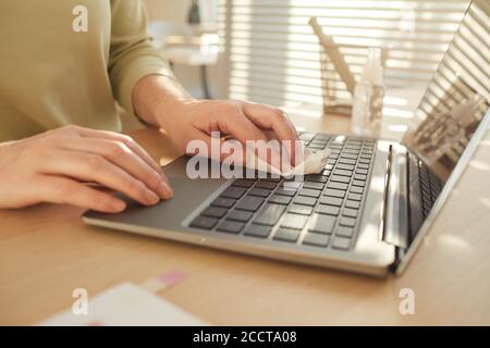 Close up pf unrecognizable woman sanitizing laptop while working at desk in post pandemic office lit by sunlight, copy space Stock Photo