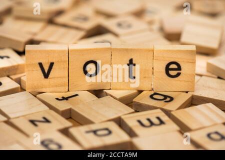 Wooden letters composing the word 'vote' on a background of scattered letters spilled on a wooden board