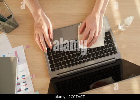 Above view close up pf unrecognizable woman sanitizing laptop while working at desk in post pandemic office lit by sunlight, copy space Stock Photo