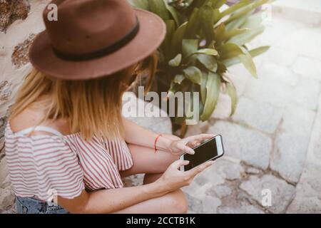 Unrecognizable woman sitting with hat watching her mobile phone Stock Photo