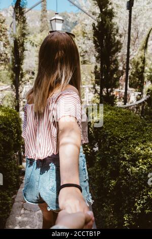 Back view of blonde woman holding hands and walking in a nature park Stock Photo
