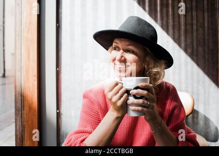 portrait of a woman smiling whilst drinking coffee in a cafe Stock Photo