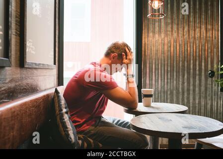 man sat feeling stressed with his face in his hands in a cafe Stock Photo