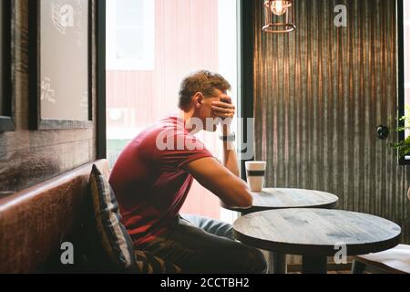 man sat covering his face feeling stressed whilst sat in a cafe Stock Photo