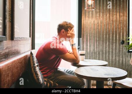 man sat covering his face looking stressed whilst in a cafe drinking Stock Photo