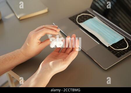 Closeup pf unrecognizable woman sanitizing hands while working at desk in post pandemic office, copy space Stock Photo