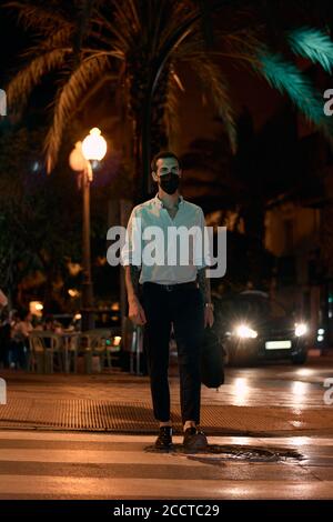 Young businessman walks down the street wearing a mask at night Stock Photo