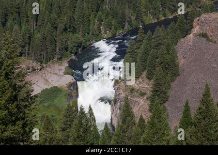 Lower Mesa Falls in Idaho along the Mesa Falls Scenic Byway on a bright sunny day with wild and fast water cascading down rock cliffs with surrounding Stock Photo