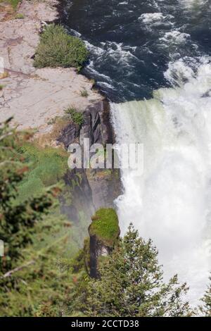 Lower Mesa Falls in Idaho along the Mesa Falls Scenic Byway on a bright sunny day with wild and fast water cascading down rock cliffs with surrounding Stock Photo