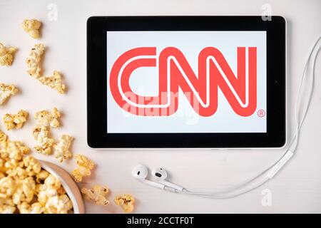 CNN logo on the screen of the tablet laying on the white table and sprinkled popcorn on it. Apple earphones near the tablet showing a CNN app, August Stock Photo