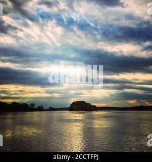Beauitiful sunset sky over the water. Dramatic clouds and bright sunbeams. Stock Photo
