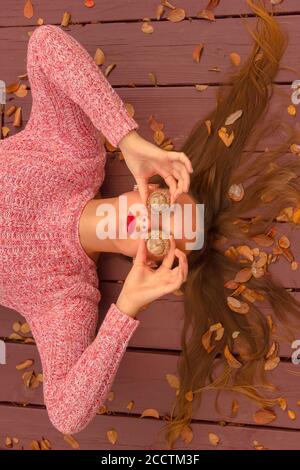 Where is fall ? Young woman lying on a wooden deck, covering her eyes with huge acorns. Stock Photo
