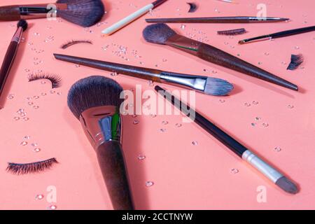 brushes for makeup of different sizes on a pastel background, accompanied by false eyelashes and small diamonds distributed by the set, top and close Stock Photo