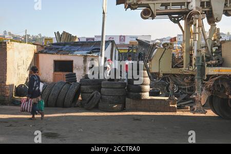 Fianarantsoa, Madagascar - May 06, 2019: Old tires by the road at the local garage repair workshop, construction vehicle on the right. Only few roads Stock Photo