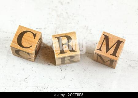 Three wooden cubes with letters CRM - stands for Customer relationship management - on white board. Stock Photo