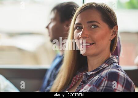 Candid portrait - young woman in shirt sitting in the bus, smiling, blurred man behind her, detail on her face Stock Photo