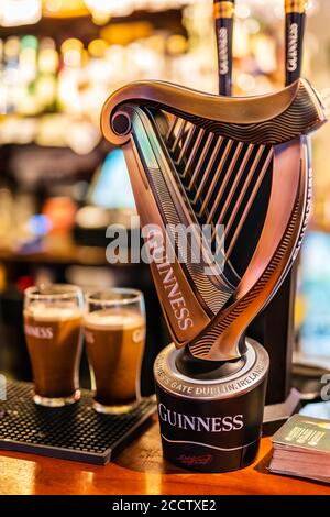 Dublin, Ireland, August 2018 Selective focus on Guinness tap with blurred pints of foamy beer and wall of bottles. Guinness is iconic Irish beer Stock Photo