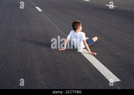 boy sits on  carriageway ,safety of children on  roadway, traffic rules concept, deadly threat Stock Photo