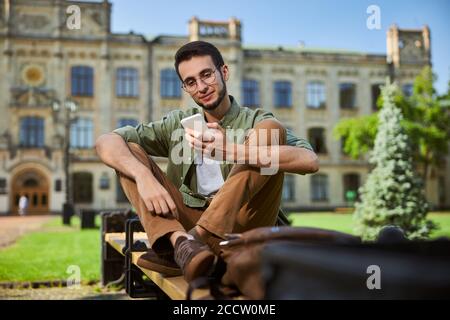 Focused student in eyeglasses staring at his cellphone Stock Photo