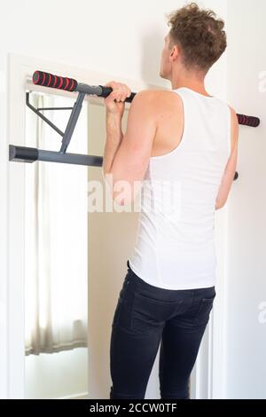 Slim athletic male performing chin up exercise in doorway, using a supinated or underhand grip primarily activating the biceps and lats. Home workout. Stock Photo