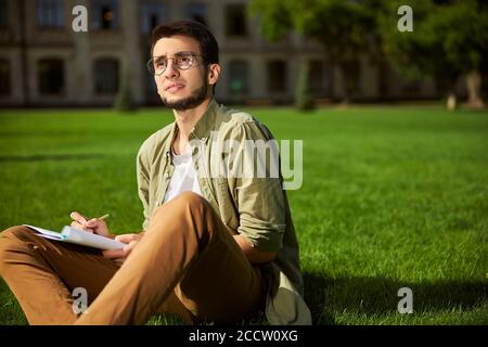 Pensive student in eyeglasses sitting on the grass Stock Photo