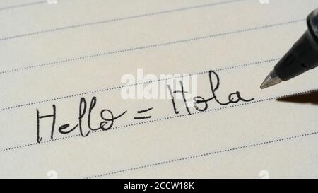 Beginner Spanish language learner writing Hello word Hola for homework on a notebook macro shot Stock Photo