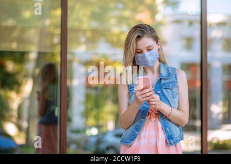 Young Asian businesswoman with protective mask using phone near her office waiting for a taxi near a station in the city streets outdoors near a windo Stock Photo
