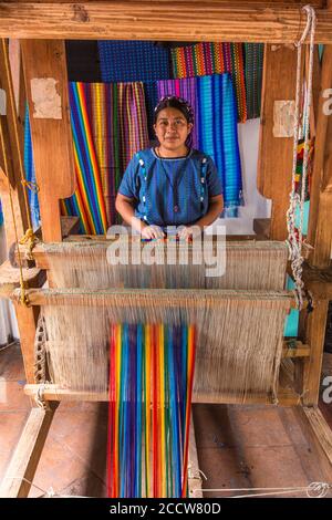A Cakchiquel Mayan woman in the traditional dress of San Antonio Palopo, Guatemala weaves colorful fabric on a traditional wooden foot-treadle loom. Stock Photo